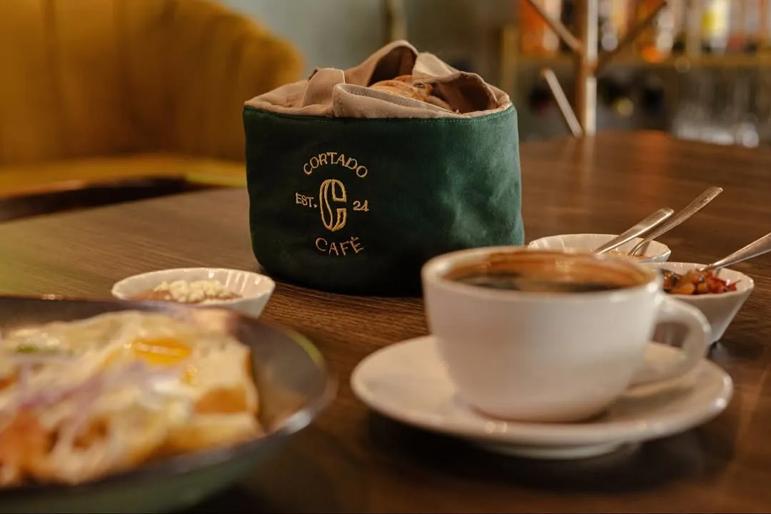 Mesa con taza de café y una bolsa verde con pan